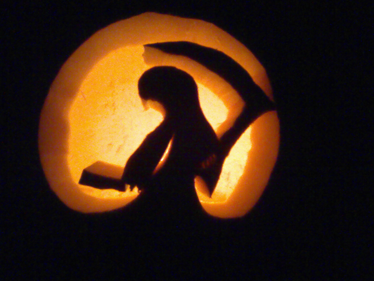 Pumpkin carving of a grim reaper from afar, the cloaked figure holding their scythe at the ready.