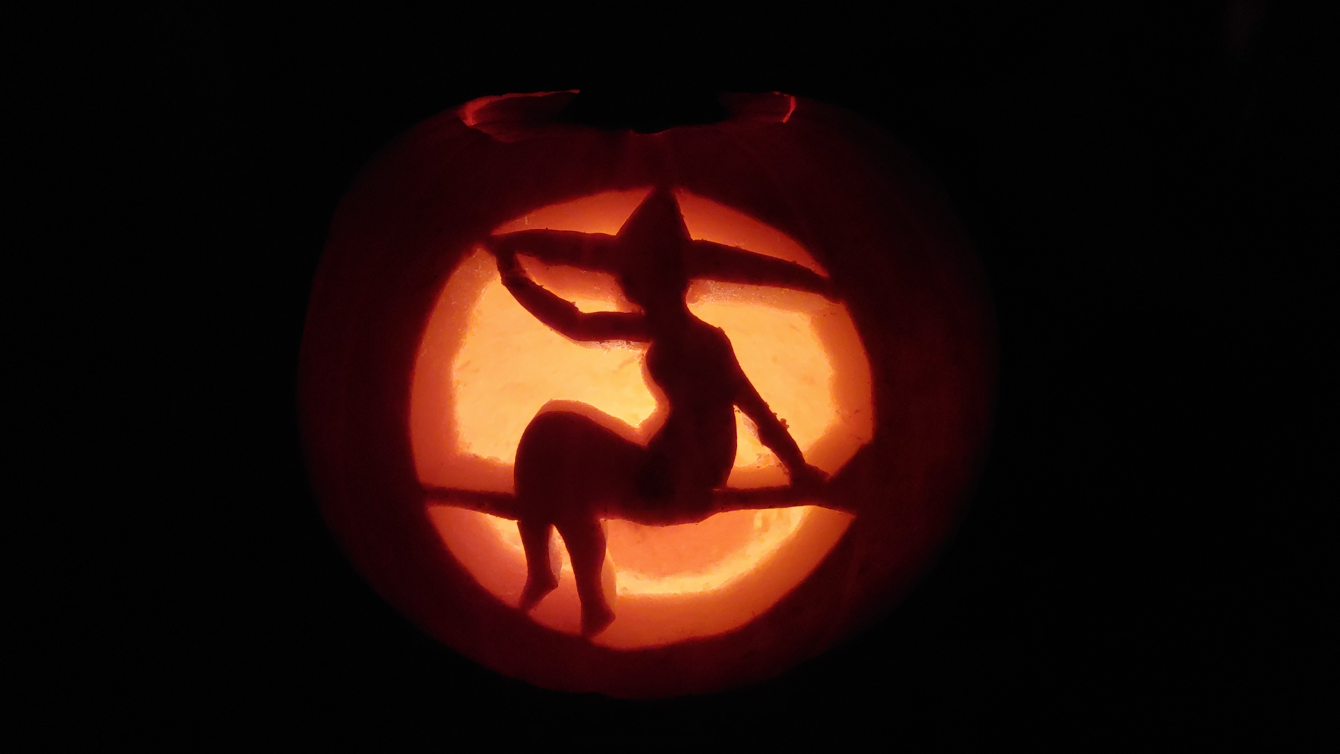Pumpkin carving of a witch on a broom in silhouette.